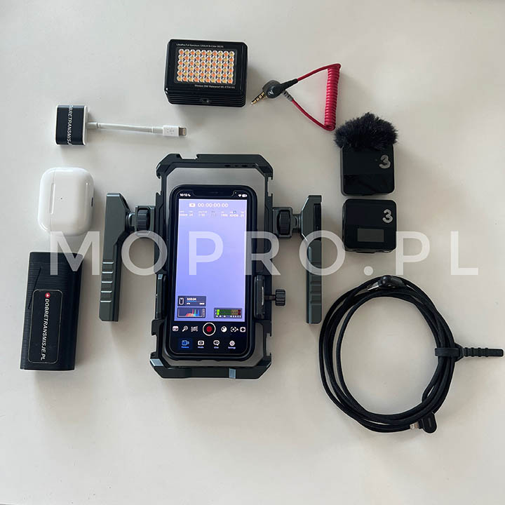 Smartfon w klatce reporterskiej (rig), wokół niego akcesoria do mobilnej produkcji: mikrofon, lampa, słuchawki, zasilanie